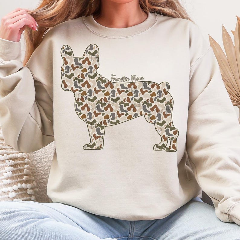 A woman wearing a white sweatshirt with a camouflage dog design on it.