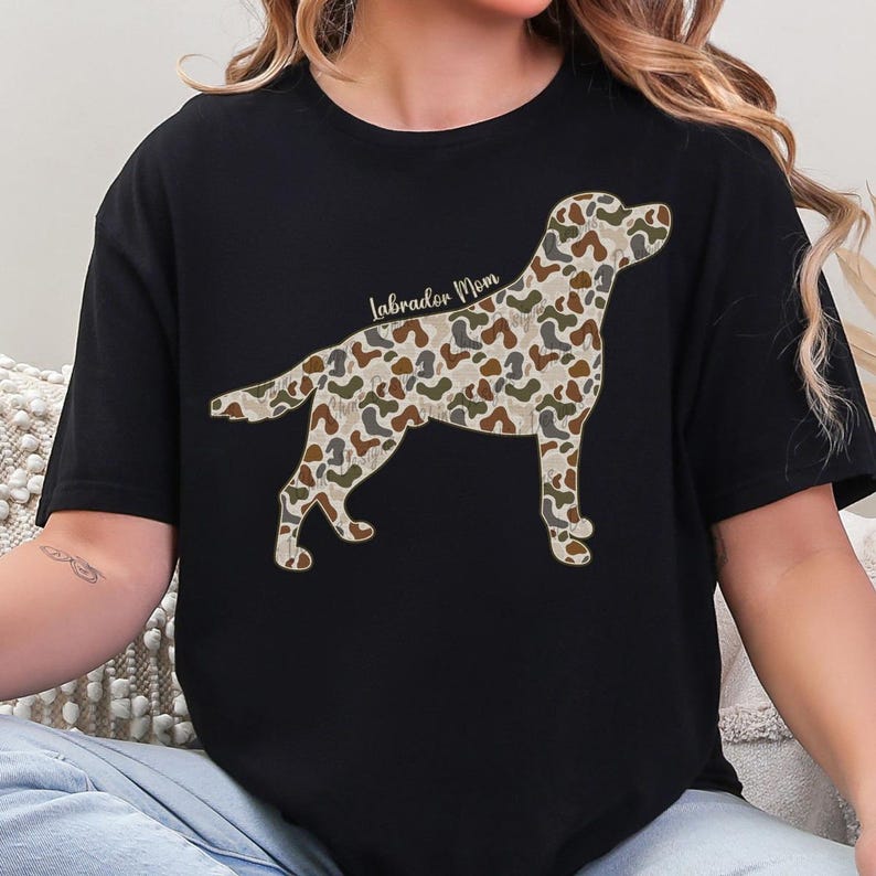 A black t-shirt with a camouflage pattern of a dog, specifically a Labrador Retriever, printed on it.