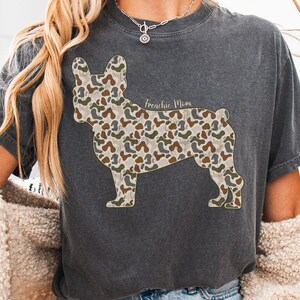 A person wearing a gray t-shirt with a camouflage dog design and a necklace.
