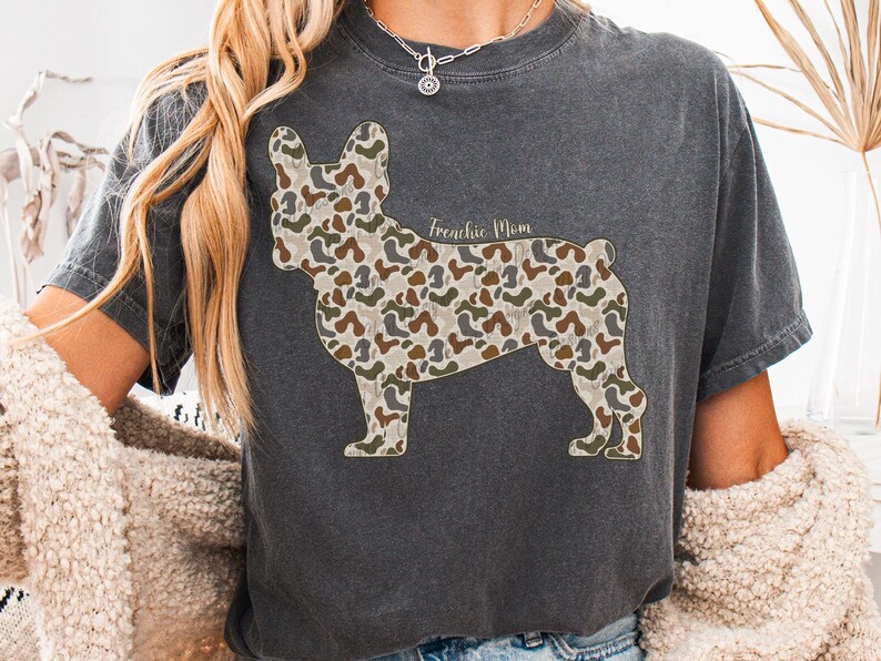 A person wearing a gray t-shirt with a camouflage dog design and a necklace.