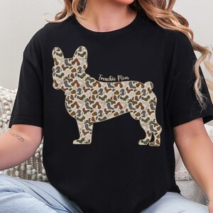 A woman wearing a black t-shirt with a camouflage pattern of a dog, specifically a French Bulldog, printed on it.