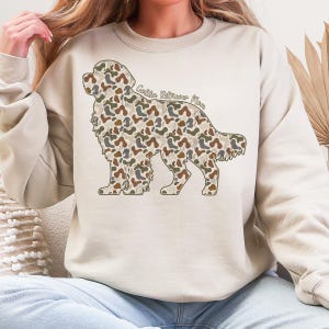 A woman wearing a beige sweatshirt with a camouflage dog design on it.