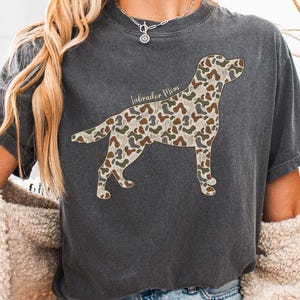 A person wearing a gray t-shirt with a camouflage dog design and a necklace.