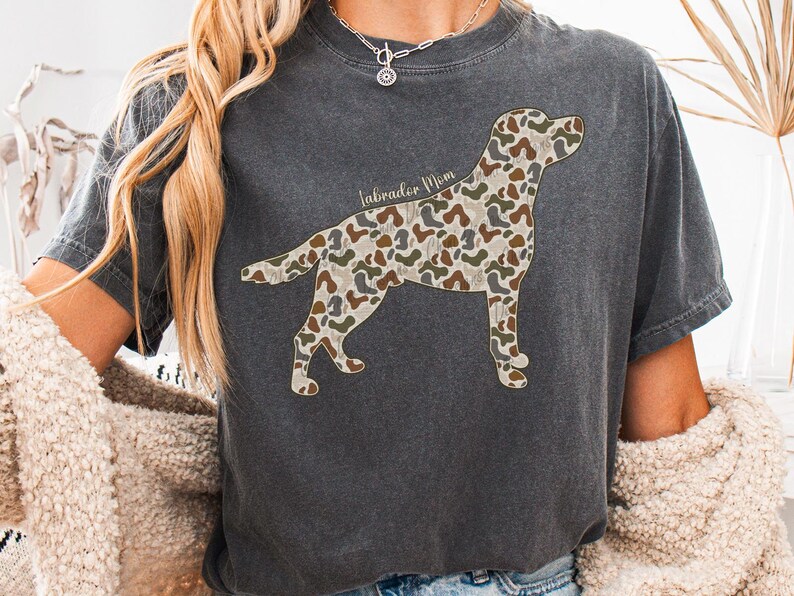 A person wearing a gray t-shirt with a camouflage dog design and a necklace.