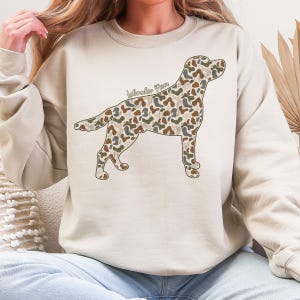 A woman wearing a white sweatshirt with a camouflage dog design on it.