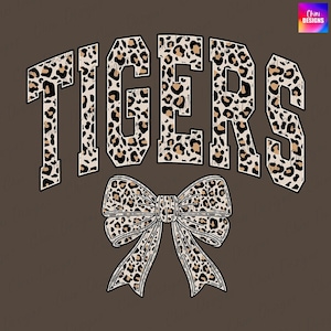 May include: Brown graphic design featuring the word "TIGERS" in large, bold letters with a leopard print pattern. Below the word is a large bow with the same leopard print design. The background is a solid brown color.