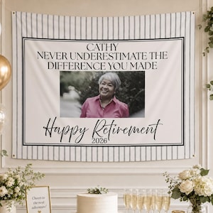 以下が含まれることがあります： 女性の写真と「Cathy, Never Underestimate the Difference You Made, Happy Retirement 2026」というテキストが入った退職バナー。バナーは白黒のストライプです。ケーキ、シャンパン、花がテーブルにあります。