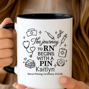 Puede incluir: Taza de cerámica blanca con interior y asa negros. La taza presenta dibujos lineales negros de símbolos médicos y el texto "The journey to RN begins with a pin Kaitlyn Nurse Pinning Ceremony 12.01.26."
