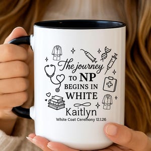 May include: White ceramic mug with a black interior and handle. The mug features the text "The journey to NP begins in white" along with medical-themed illustrations and the name "Kaitlyn". The bottom of the mug reads "White Coat Ceremony 12.1.26".