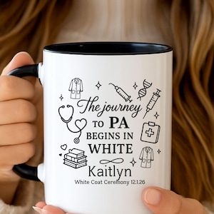 Puede incluir: Taza de cerámica blanca con interior y asa negros. La taza presenta el texto "The journey to PA begins in white" con ilustraciones médicas y el nombre "Kaitlyn".
