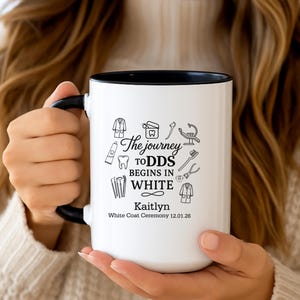 May include: White ceramic mug with a black interior and handle. The mug features the text "The journey to DDS begins in WHITE" with dental-themed illustrations. The name "Kaitlyn" and the date "12.01.26" are also printed on the mug.