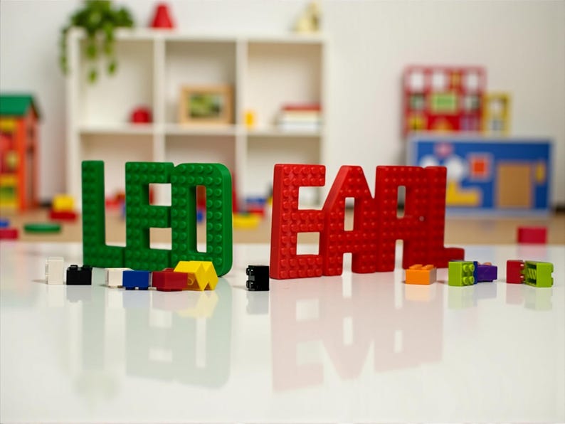 May include: Green and red building block letters spell out the word "LEGO" and "EAR". Various colorful building blocks are scattered on a white surface. The background includes a white shelf with toys.
