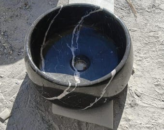 Può includere: Un lavabo rotondo in marmo nero con venature bianche. Il lavabo ha una finitura liscia e lucida e un foro di scarico circolare al centro.