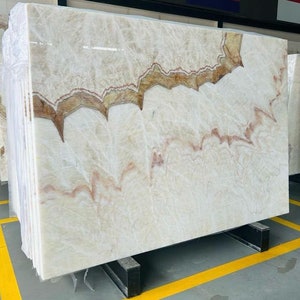 Puede incluir: Una gran losa de ónix blanco con vetas marrones y rojas. La piedra tiene un patrón natural y orgánico.