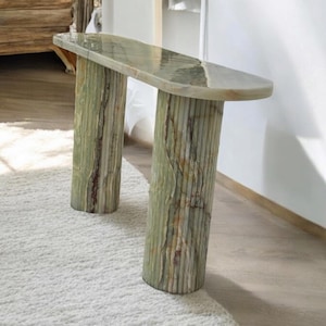 以下が含まれることがあります： 緑のオニキスのコンソールテーブル。楕円形の天板と2本の溝のある脚が付いています。テーブルは白い敷物の上に置かれています。