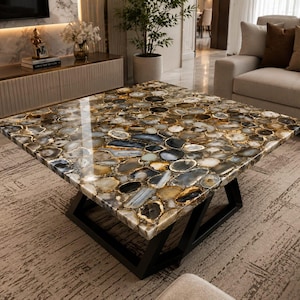 May include: A square coffee table featuring a polished tabletop composed of numerous multicolored agate slices in shades of brown, gray, and white, supported by a sturdy black metal base with an angular, geometric frame design.