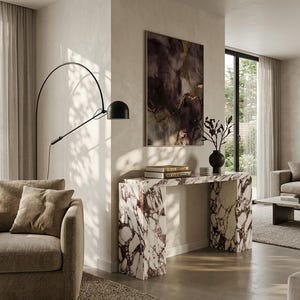 May include: A modern living room featuring a marble console table with a burgundy and white pattern. A black arched floor lamp and a framed abstract painting are also visible. Two books are on the table, and a sofa with brown cushions is in the foreground.