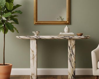 May include: A rectangular console table crafted from white marble with prominent grey and black veining, featuring a smooth, rounded top surface supported by two thick, matching marble legs. The table is positioned horizontally.