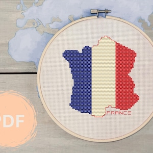May include: A cross-stitch pattern of the outline of France with the French flag colors, blue, white, and red, and the word "FRANCE" below the outline.