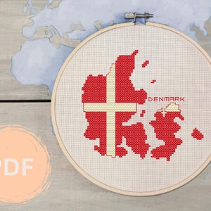 Könnte beinhalten: Kreuzstich-Stickerei der Karte von Dänemark in Rot und Weiß, in einem hölzernen Stickrahmen. Das Wort "DENMARK" ist rot gestickt. Das PDF-Symbol befindet sich in der unteren linken Ecke.