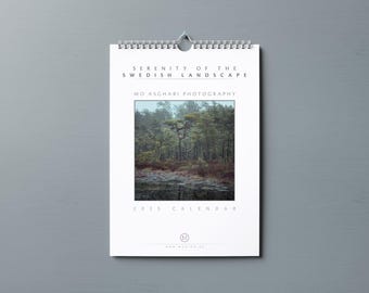May include: A white calendar featuring a photograph of a misty forest scene. The text "Serenity of the Swedish Landscape" and "Mo Asghari Photography" are printed at the top. The calendar is for the year 2023.