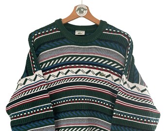 May include: A green, blue, red, and white striped sweater with a crocodile logo. The sweater has a crew neck and long sleeves.