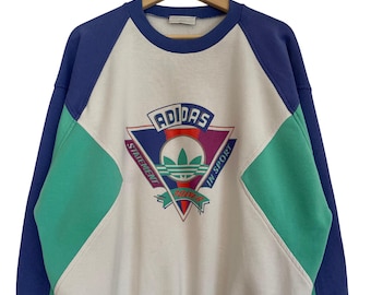 May include: A vintage Adidas sweatshirt in white, blue, and green. The sweatshirt features a large Adidas logo in a triangle with the words "STATEMENT" and "IN SPORT". The sleeves and shoulders are blue, with green panels on the front.