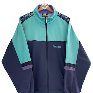 Könnte beinhalten: Eine blaue und türkisfarbene Vintage-Trainingsjacke mit Reißverschluss und dem Aufdruck "ASICS" auf der Vorderseite. Die Jacke hat einen hohen Kragen und ein gestreiftes Muster an den Ärmeln.