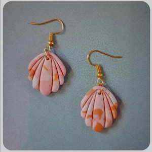 Könnte beinhalten: Ein Paar ohrringförmige Muscheln. Die Ohrringe haben ein rosa, weißes und orangefarbenes Marmormuster. Die Ohrhaken und die Verbindungshardware sind goldfarben.
