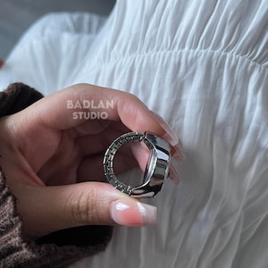 Puede incluir: Un anillo de reloj plateado con una esfera redonda y una banda plateada. La banda est&aacute; hecha de peque&ntilde;as piezas enlazadas que se asemejan a una cadena.