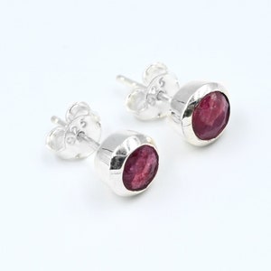 May include: A pair of silver stud earrings with red ruby gemstones. The earrings are marked with "925" on the back.