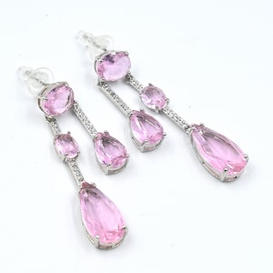 Può includere: Un paio di orecchini pendenti con cristalli rosa a forma di goccia e dettagli argentati.
