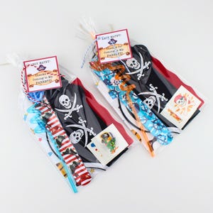 May include: Two clear plastic favor bags filled with pirate-themed party supplies, including black capes with white skull and crossbones, colorful slap bracelets, and temporary tattoos. Each bag is sealed with a tag reading AHOY MATEY! Thanks for Coming to My PARRRTY! with a small pirate hat graphic.