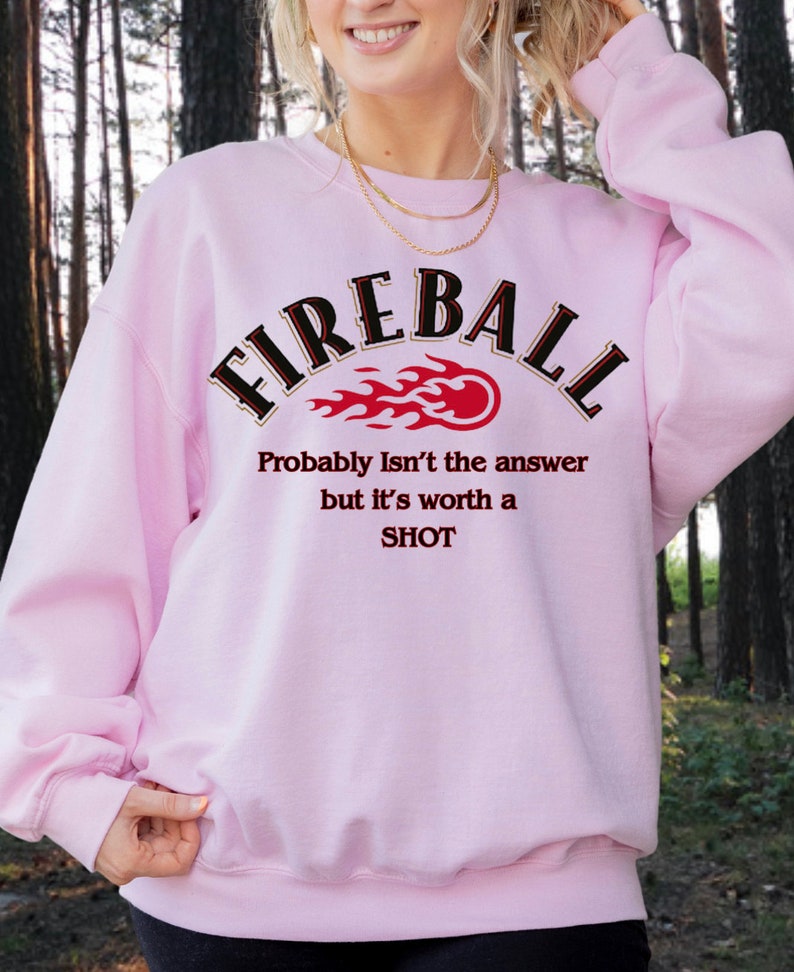 May include: Pink sweatshirt with the text "FIREBALL" in black with a red and orange flame graphic. The text "Probably Isn't the answer but it's worth a SHOT" is printed below the graphic.