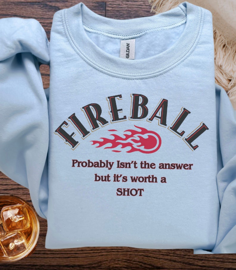 May include: Light blue sweatshirt with the text "FIREBALL" in a black and gold arch with a red flame graphic. The text "Probably Isn't the answer but it's worth a SHOT" is printed below the graphic.