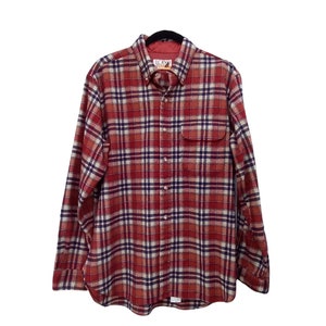Może przedstawiać: Flanelowa koszula w kratę w kolorze czerwonym i białym, z długimi rękawami i zapinaną na guziki. Koszula ma kieszeń na lewej piersi i metkę z napisem "L.L.Bean" z przodu.