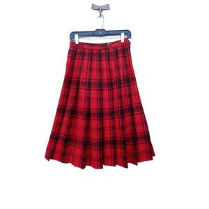 May include: A red and black plaid skirt with pleats. The skirt is hanging on a black hanger.