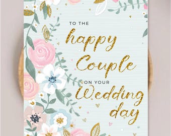 May include: A rectangular greeting card with a light blue background featuring a floral border of pink roses and white flowers. The text reads TO THE happy Couple ON YOUR Wedding day in gold glitter script and black sans-serif font.