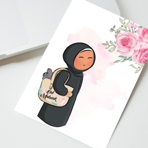 May include: A cartoon illustration of a person wearing a black hijab and carrying a beige tote bag with the text "Eid Mubarak" on it. The bag has a pink floral design and a gray cat peeking out of the top. The background is a watercolor wash of pink and white.