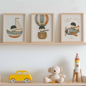 Könnte beinhalten: Drei gerahmte Wandbilder mit Illustrationen eines Kindes in einem Segelboot, einem Heißluftballon und einem Flugzeug. Darunter auf einem Regal stehen ein gelbes Spielzeugauto, ein beiger Plüschteddy und eine weiß-rot-gelbe Spielzeugrakete.