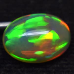 Könnte beinhalten: Ein runder, ovaler Opal-Edelstein mit einer milchig weißen Basis und Blitzen von Grün, Orange und Gelb.