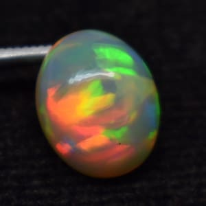 Könnte beinhalten: Ein weißer ovaler Opal-Edelstein mit einem Regenbogen aus Farben, darunter Grün, Orange und Rot.