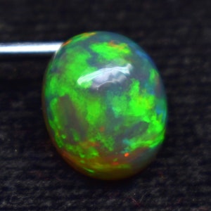 Könnte beinhalten: Ein ovaler Opal-Edelstein mit einem lebendigen Farbspiel. Der Opal hat einen durchscheinenden Körper mit grünen, orangefarbenen und blauen Lichtblitzen. Der Edelstein ist vor einem dunklen Hintergrund platziert, der seine schillernden Eigenschaften hervorhebt.