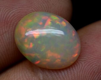 Può includere: Una pietra preziosa di opale bianco con un bagliore iridescente arancione chiaro, verde e rosso. La pietra preziosa di forma ovale misura circa 2,5 cm di lunghezza.