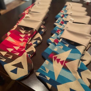 Puede incluir: Una colección de calcetines de Navidad con un patrón geométrico en tonos rojos, azules, marrones y blancos. Los calcetines están forrados con una tela beige.