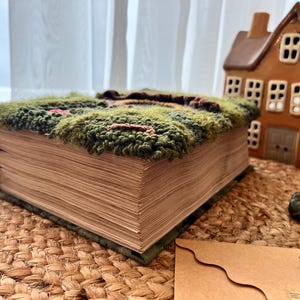 K&ouml;nnte beinhalten: Ein Buch mit einem gr&uuml;nen, braunen und roten teppichartigen Einband. Das Buch ist geschlossen und liegt auf einer geflochtenen braunen Matte.