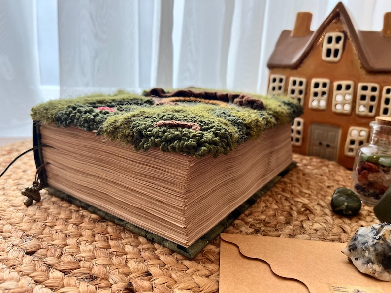 K&ouml;nnte beinhalten: Ein Buch mit einem gr&uuml;nen, braunen und roten teppichartigen Einband. Das Buch ist geschlossen und liegt auf einer geflochtenen braunen Matte.