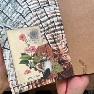 May include: A brown and white journal with a floral design and a watering can with a bird on it. The journal has a red string closure and the text "BRIGHT DAY" on the front.