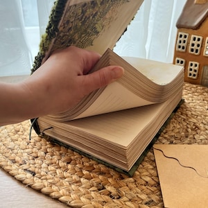K&ouml;nnte beinhalten: Ein gr&uuml;nes und braunes Journal mit einem floralen Design auf dem Umschlag. Das Journal ist ge&ouml;ffnet und zeigt leere Seiten.