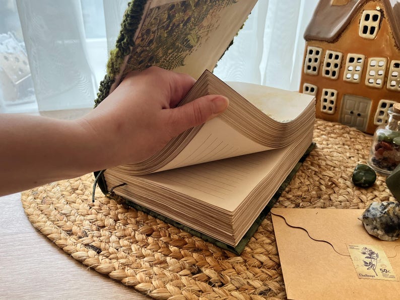 K&ouml;nnte beinhalten: Ein gr&uuml;nes und braunes Journal mit einem floralen Design auf dem Umschlag. Das Journal ist ge&ouml;ffnet und zeigt leere Seiten.